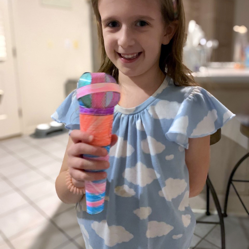 young girl smiles and holds a colorful paper microphone