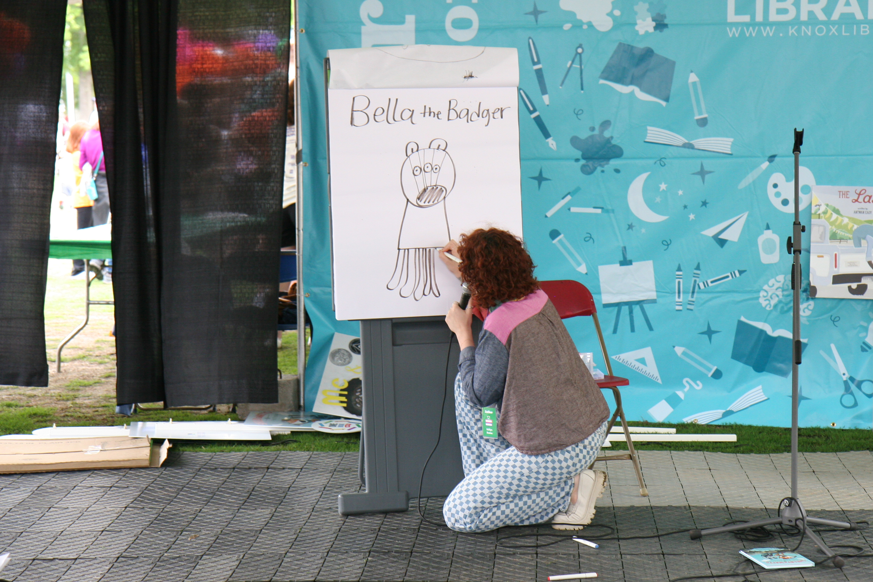 woman kneels in front easel pad where she's drawing a silly cartoon