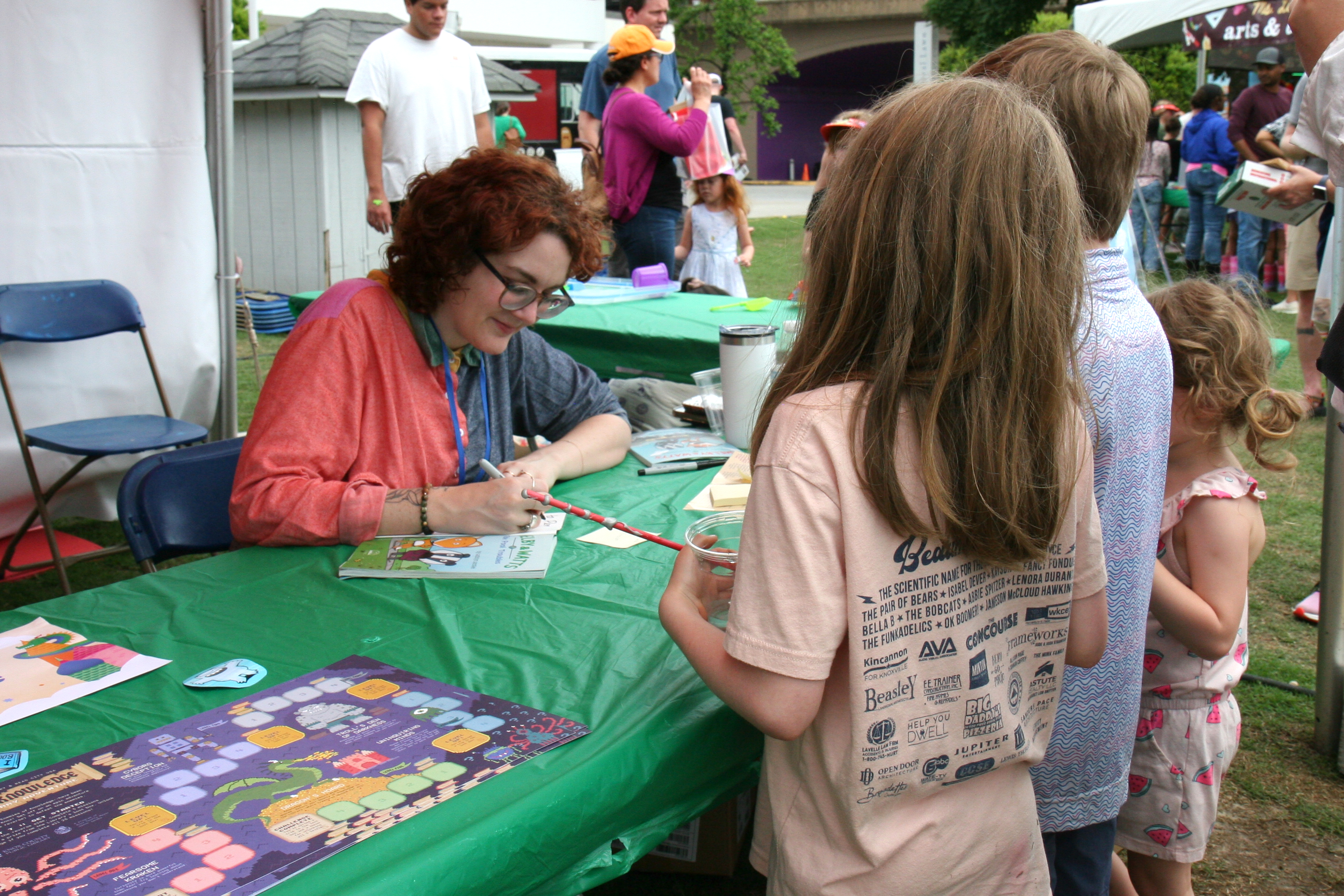 author signs a book at a table, meeting three young fans