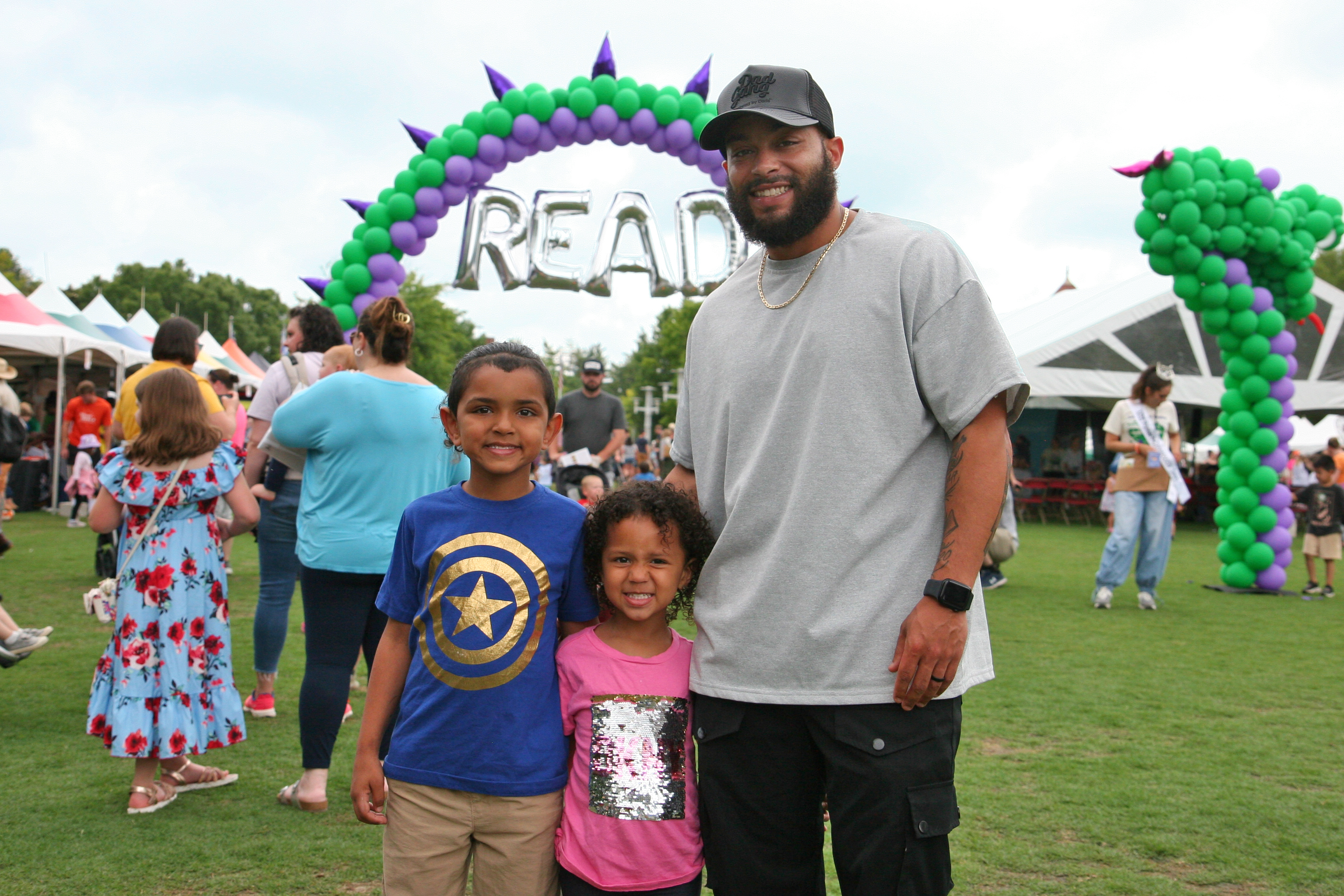 dad and two children stand in front of a dragon balloon arch with the word READ