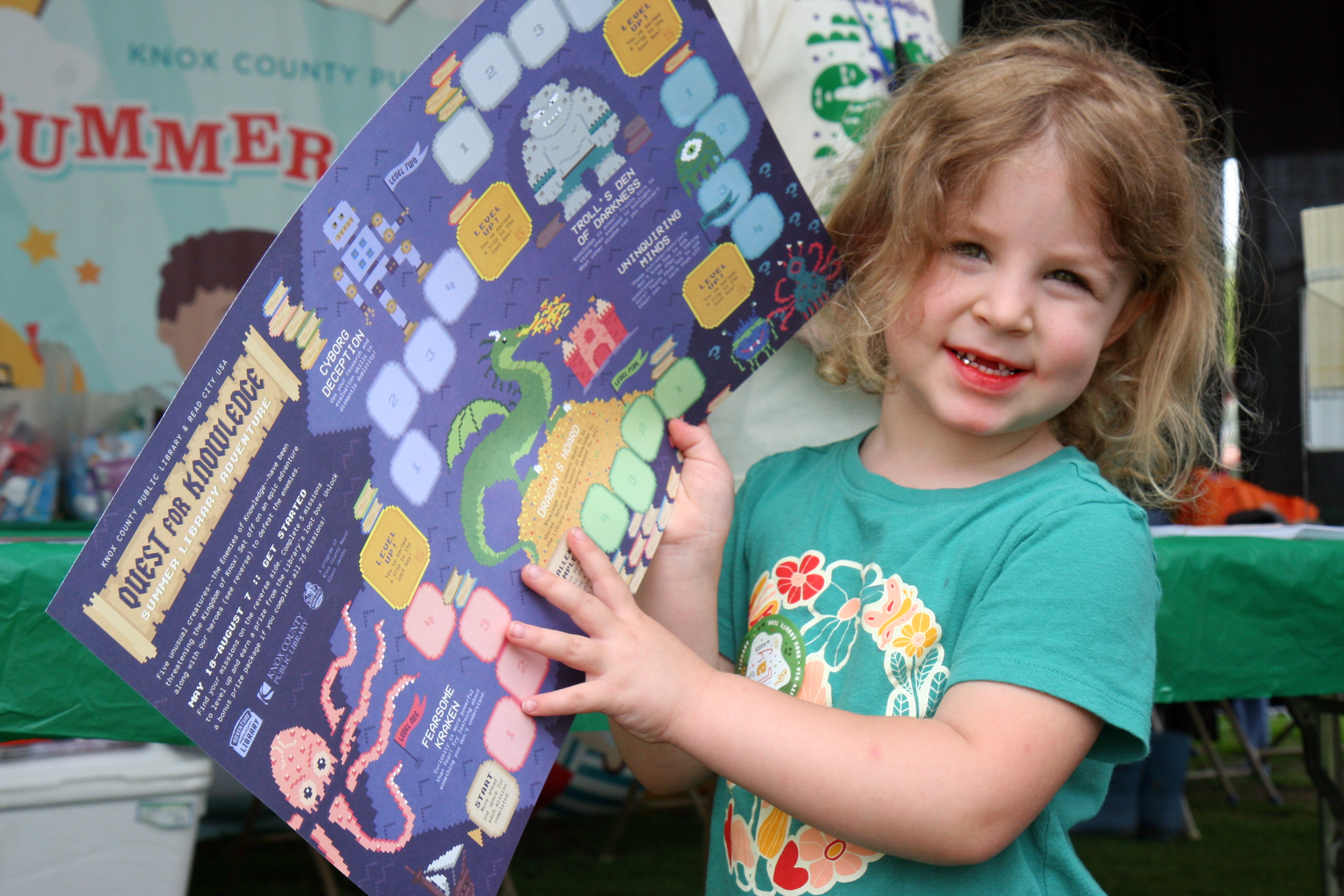 young girl points to a dragon on a large gameboard reading Quest for Knowledge