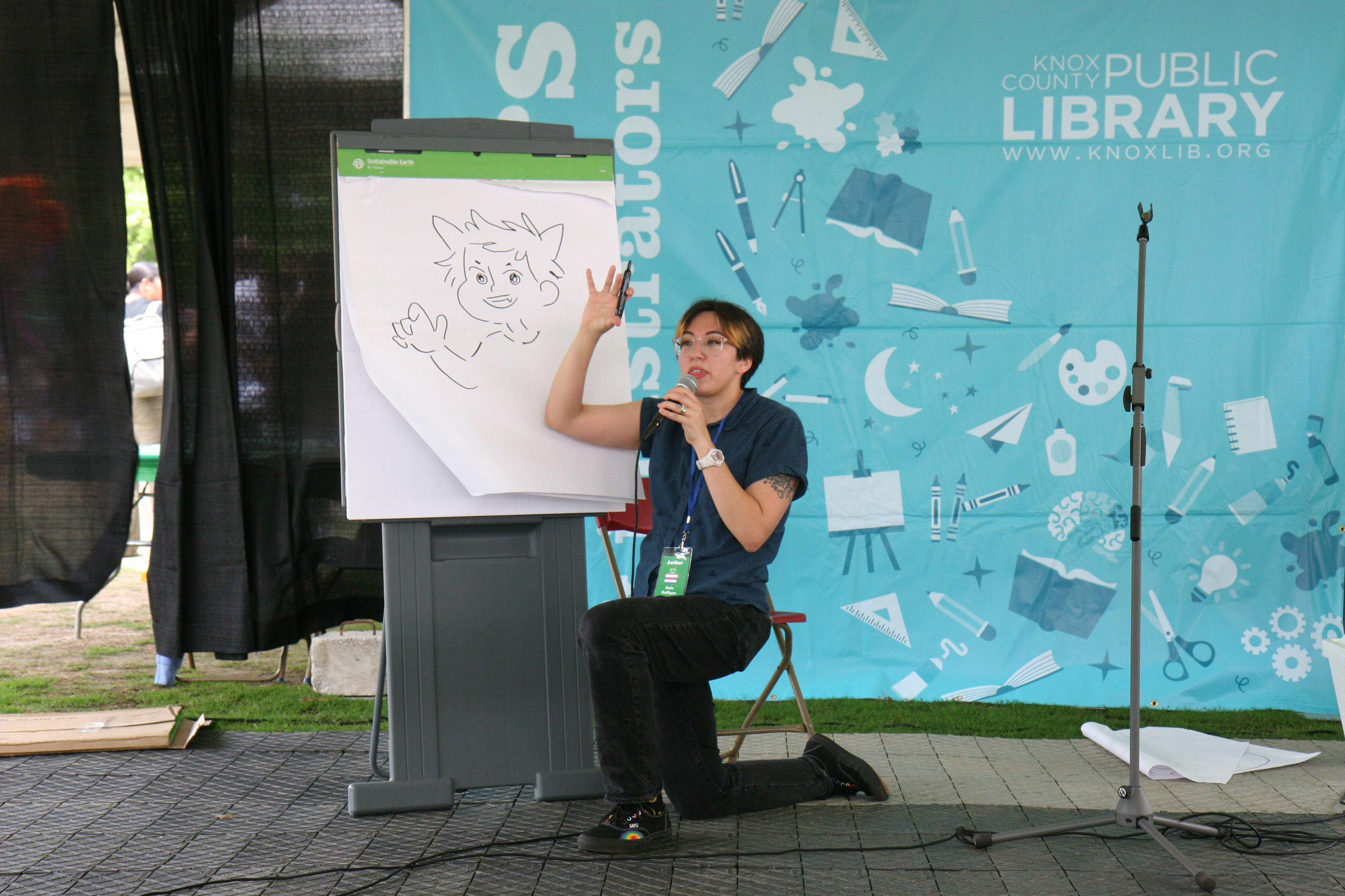 author gestures animatedly in front of an illustration on an easel pad