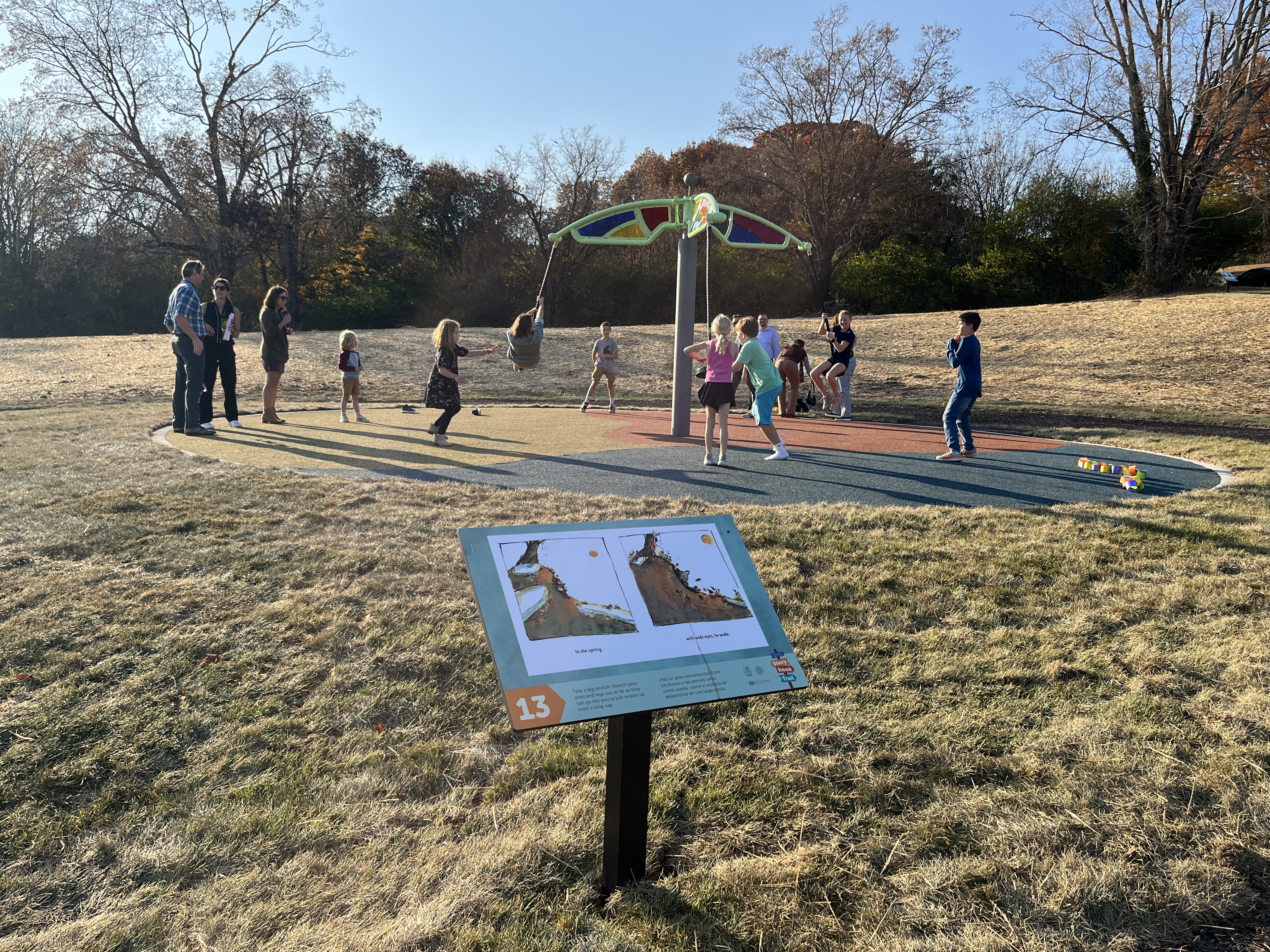 a story trail panel sits in front of a swing play structure with many kids