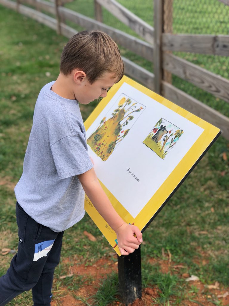 young boy leans on an outdoor story panel as he reads it