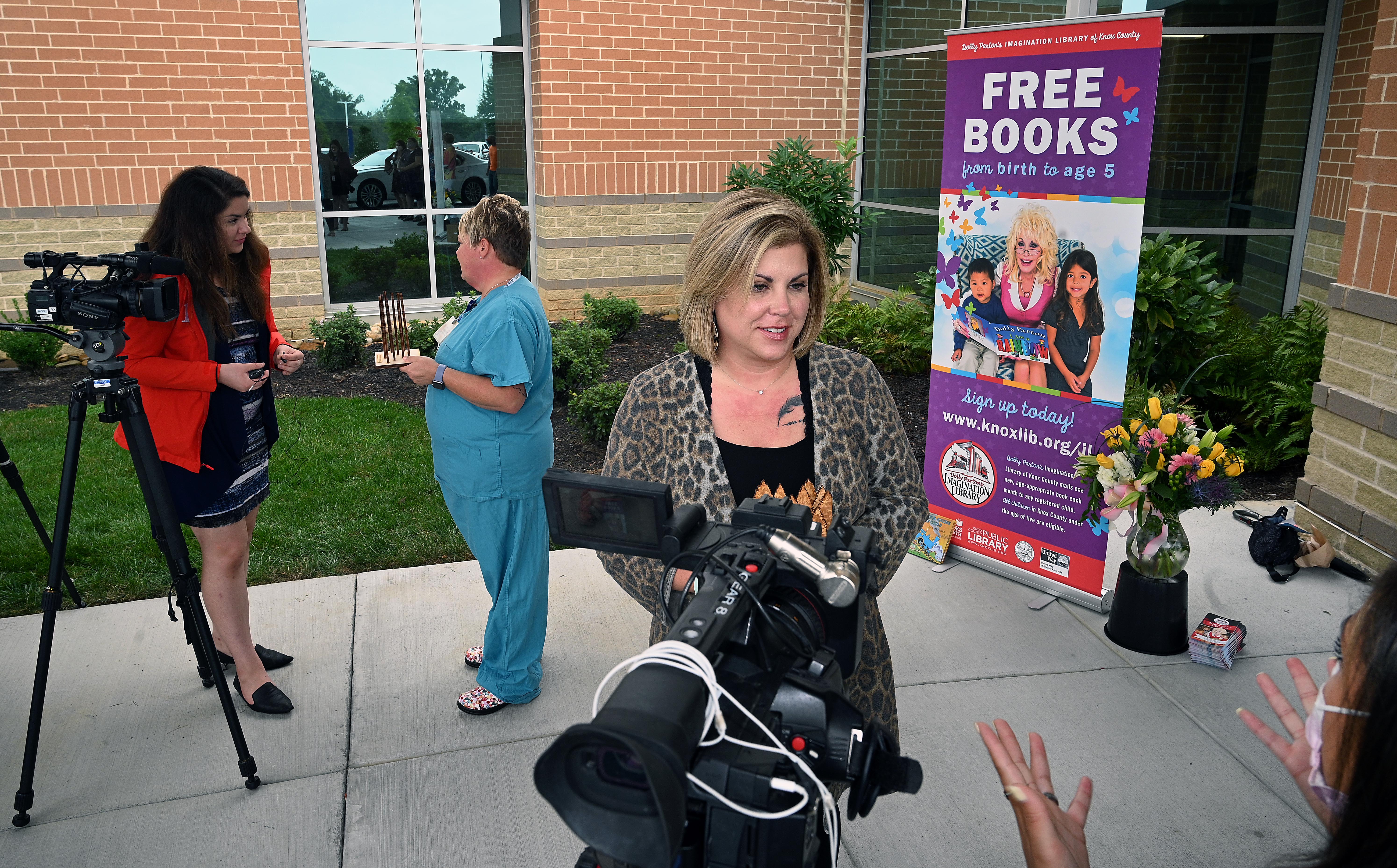 Christy Richardson (left, wearing blue scrubs and holding one half of the Seeds of Literacy award) and Holly Woodlee (right, wearing a leopard print sweater and holding the other award) are interviewed for the Seeds of Literacy Awards Ceremony 