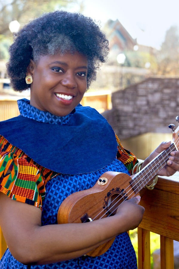 A photo of Kelle smiling and holding her ukulele on a wooden deck