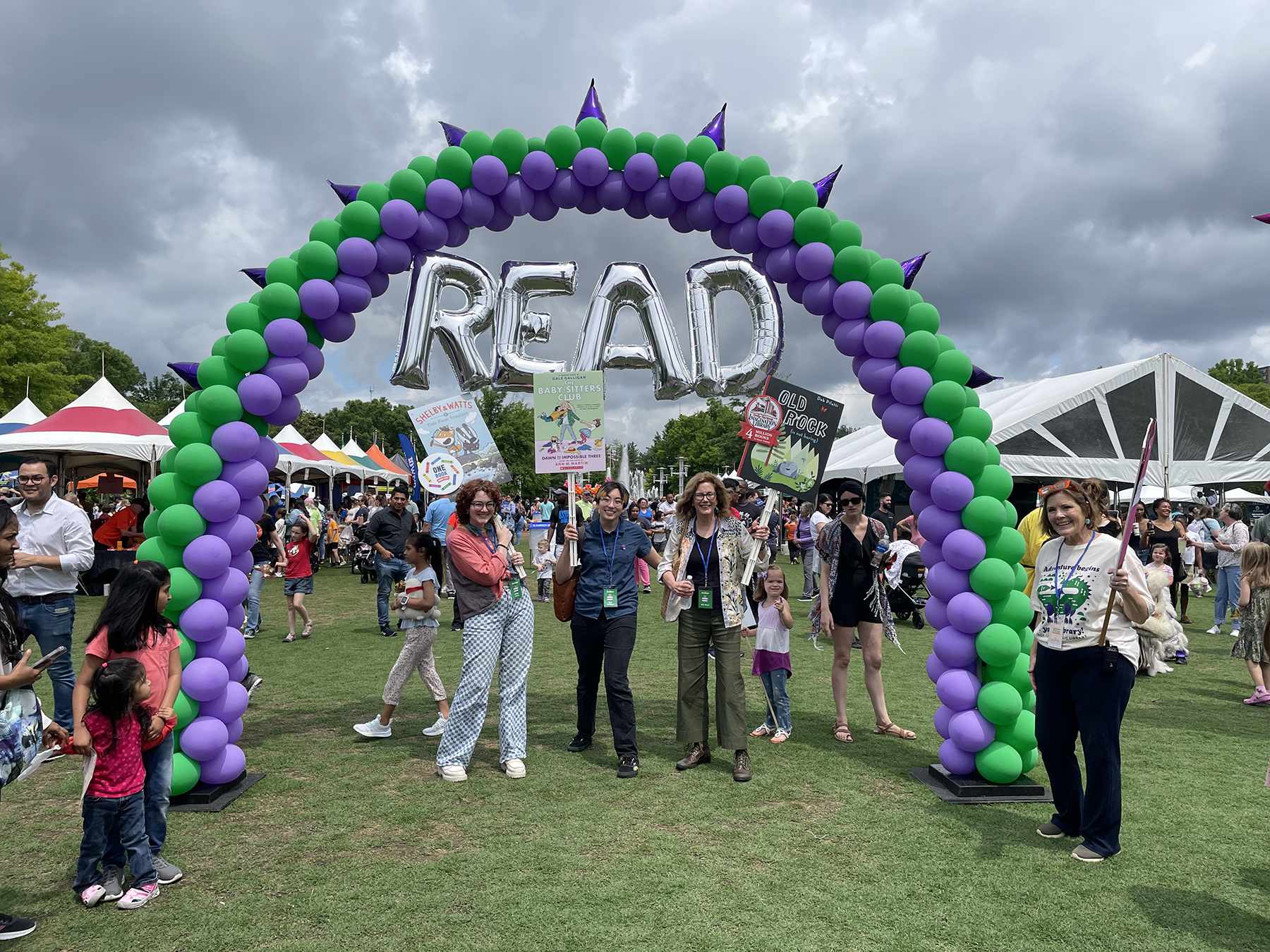 three authors hold large book covers outside under balloon arch and letters READ