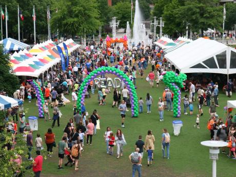 overview photo of outdoor festival with colorful tents, dragon balloon arch, large crowd, and fountain in the background