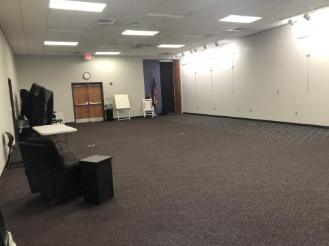 Photo shows carpeted room with covered window, padded rocking chair, wooden rocking chair, plastic stacking chairs, table with white plastic top.