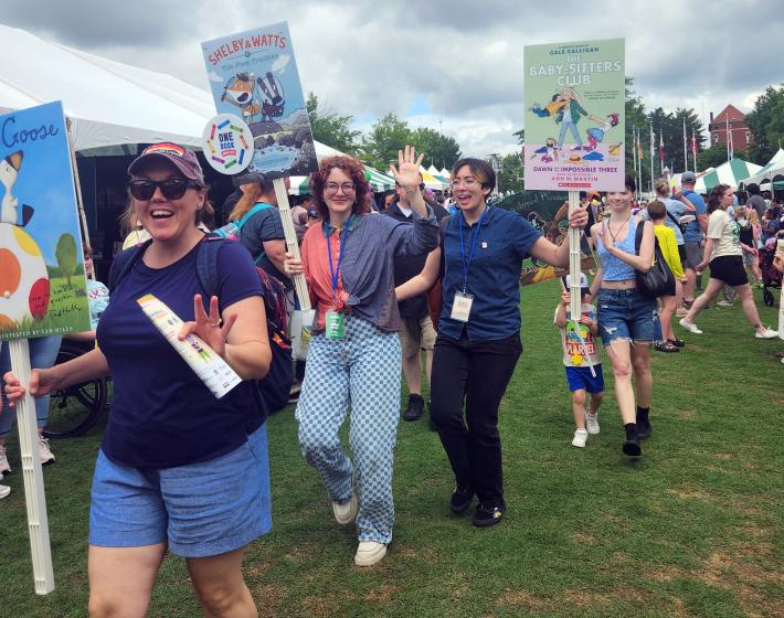 people walking in a parade, smiling, carrying signs of large children's book covers