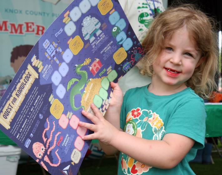 young girl holds Quest for Knowledge gameboard