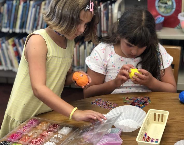 two girls working together at a table with craft supplies