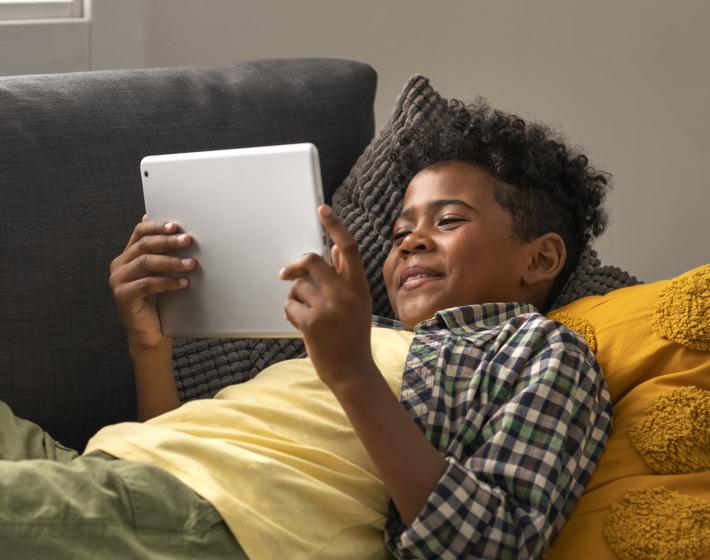 smiling boy lying on couch watching tablet