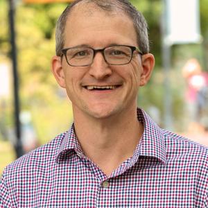 Dr Geidner wears glasses and a plaid shirt as he smiles into the camera.