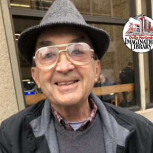 Pastor John, a slim older gentleman with glasses and a gray fedora, smiles for the camera.